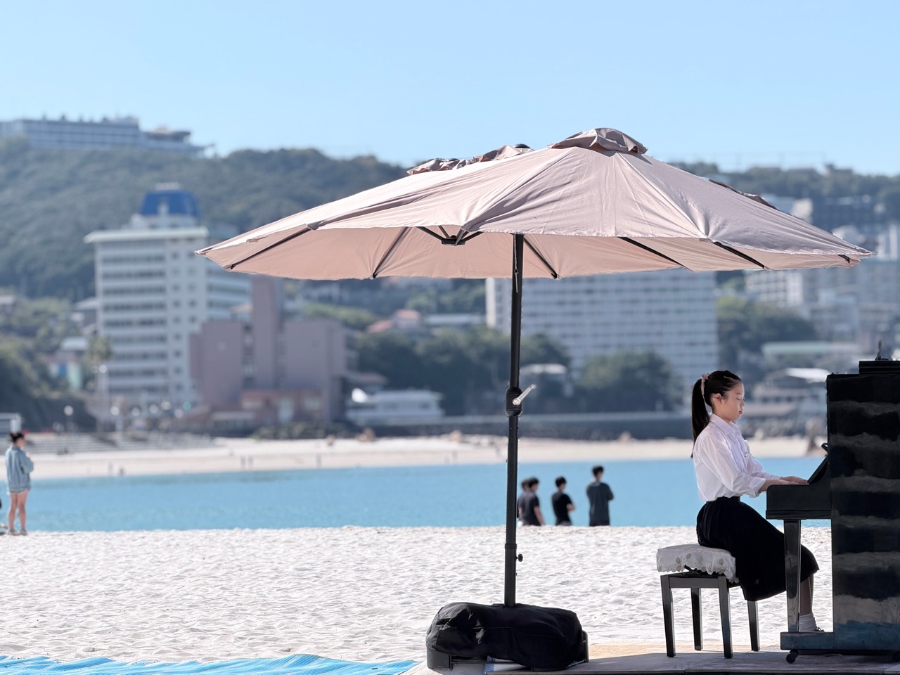 演奏者在遮阳伞下弹奏钢琴,身后是白良滨蔚蓝的大海